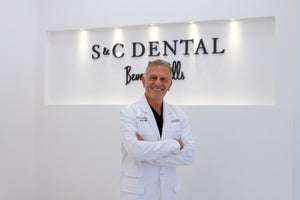 Dr Kourosh Maddahi in a white coat standing in front of an 'S & C Dental' sign.